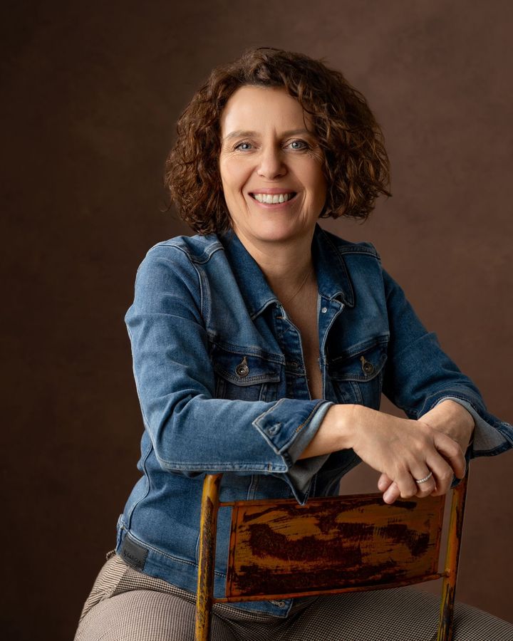 Nathalie Ghysdaal, consultante marketing créative et fondatrice de Natia, souriante, assise à califourchon sur une chaise